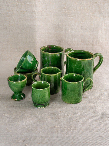 French green glazed Terre Vernissée pottery set of 8 assorted cups and mugs on textured beige fabric background.