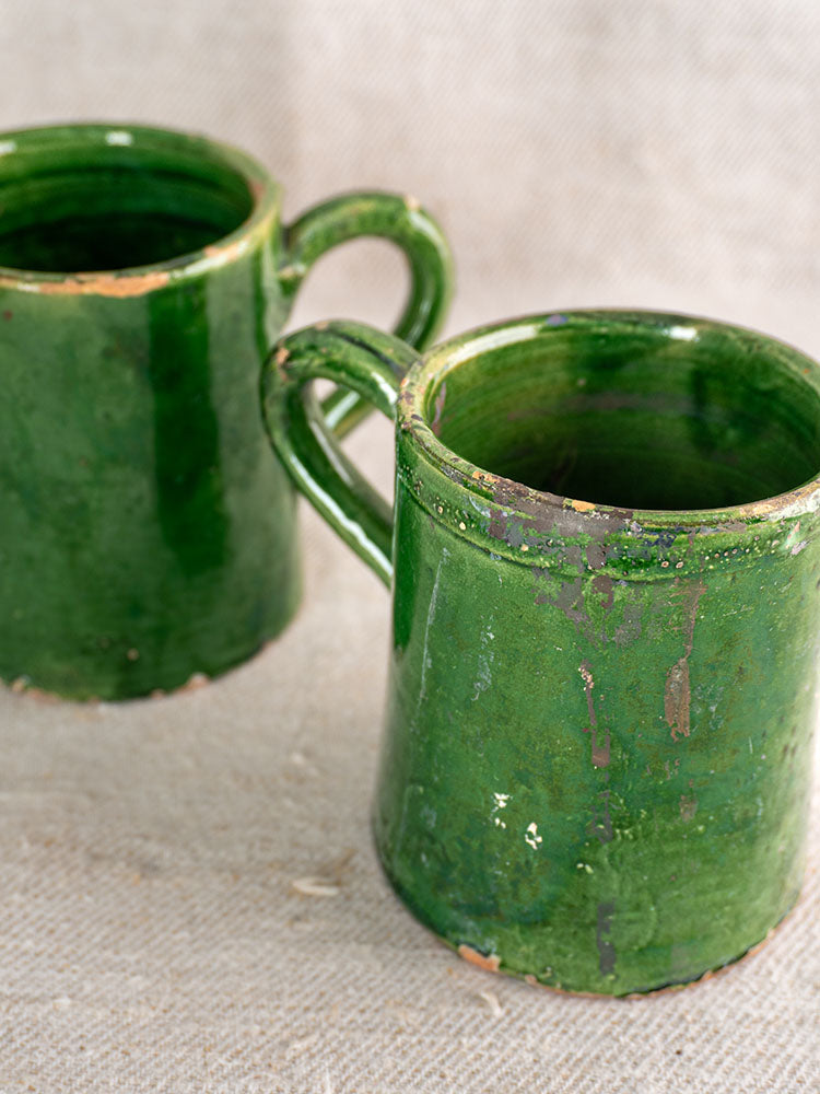 French green glazed pottery set, glossy antique finish and worn edges, arranged on textured beige fabric.