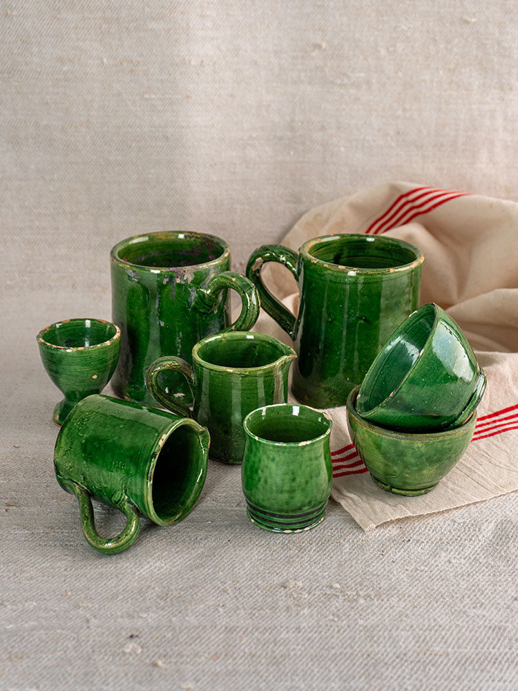 French green glazed pottery set, Provençal terre vernissée, 8 pieces, on beige textured surface with cream cloth and red stripes.