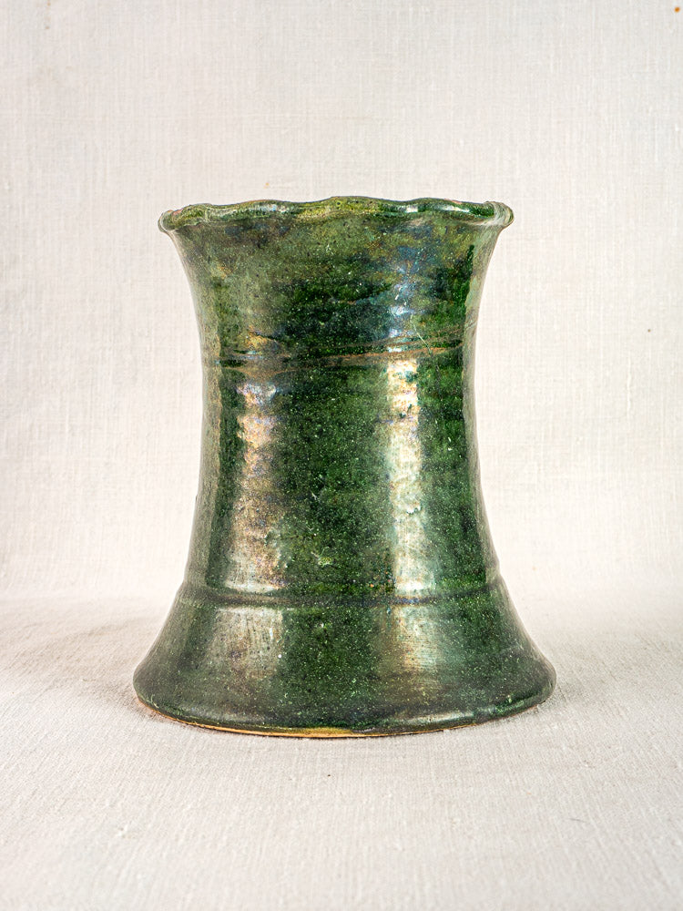 Antique French green glazed terracotta vase with wavy rim and horizontal lines on light fabric.