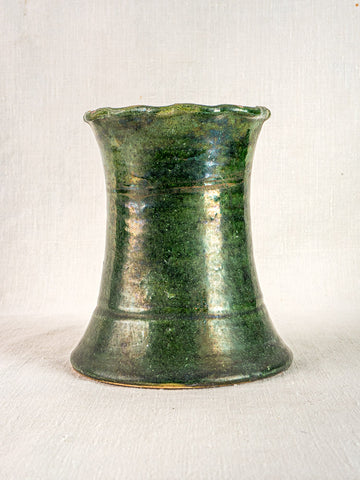 Antique French green glazed terracotta vase with wavy rim and horizontal lines on light fabric.