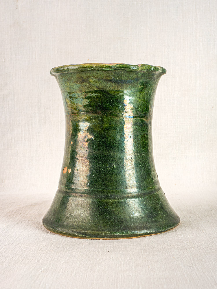 Antique French green glazed terracotta vase, hourglass shape, flared rim, on light fabric background.