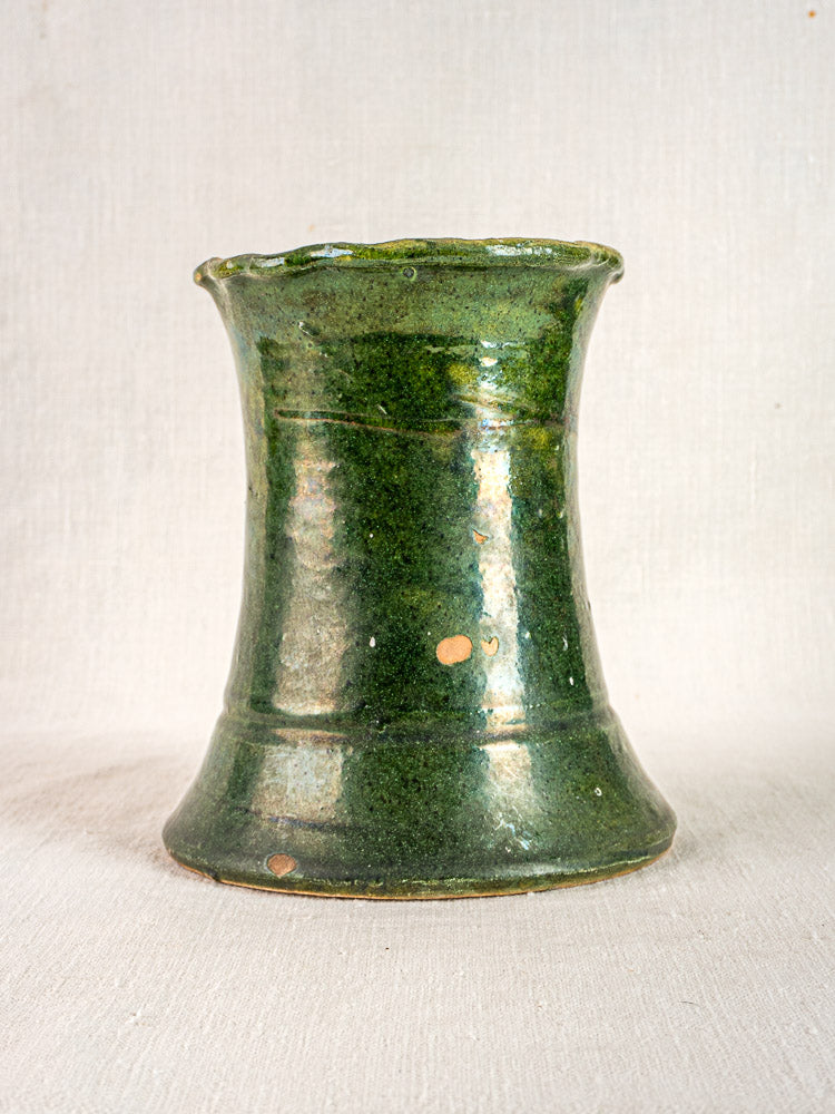 Hand-thrown antique French green glazed terracotta vase with hourglass shape, plain neutral background.