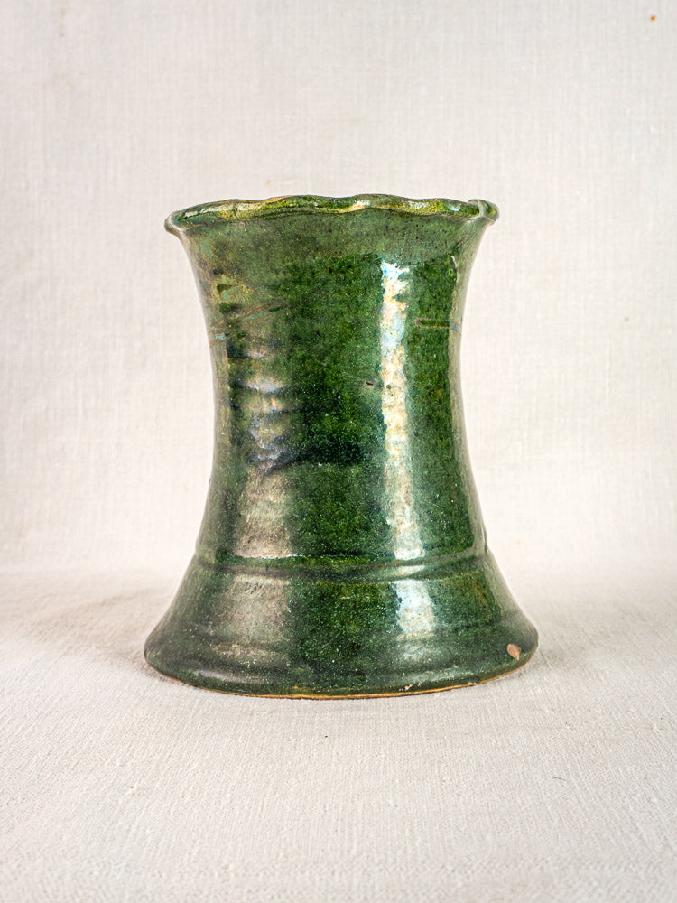 Antique French green glazed terracotta vase with flared base and rim on neutral fabric background.