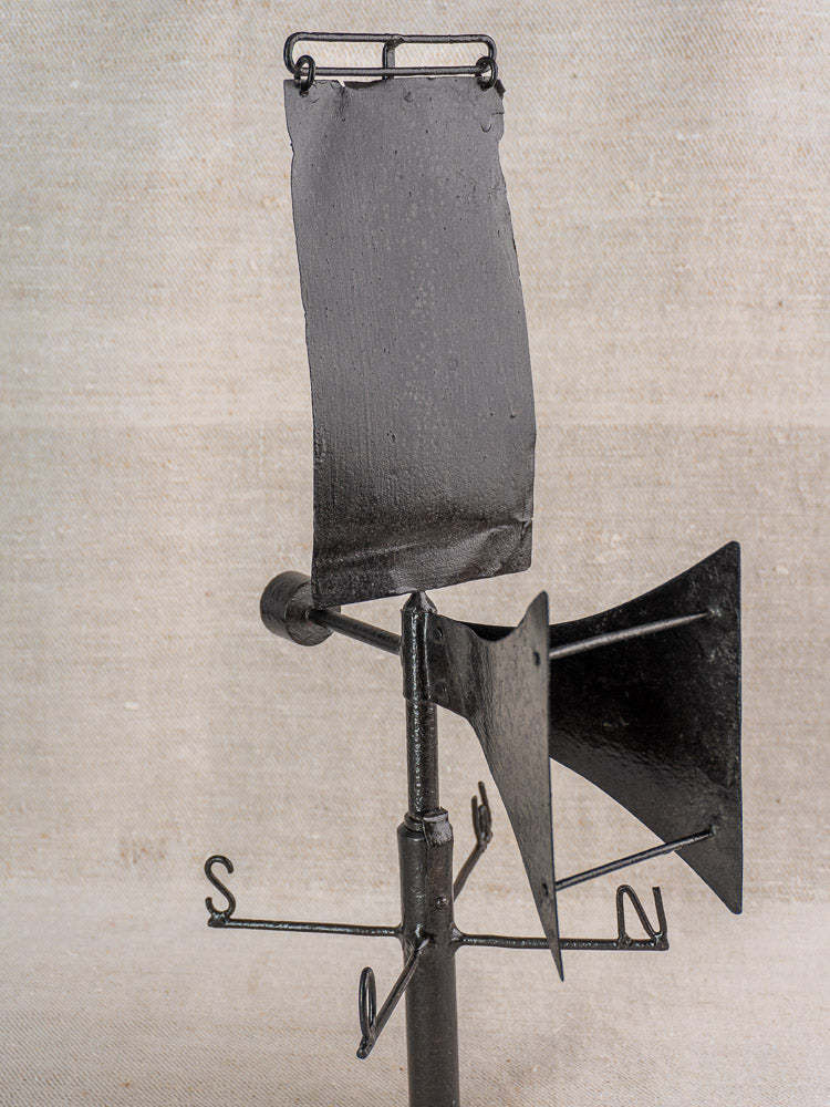 Antique French painted iron weathervane with V-shaped front, black finish, on beige fabric background.
