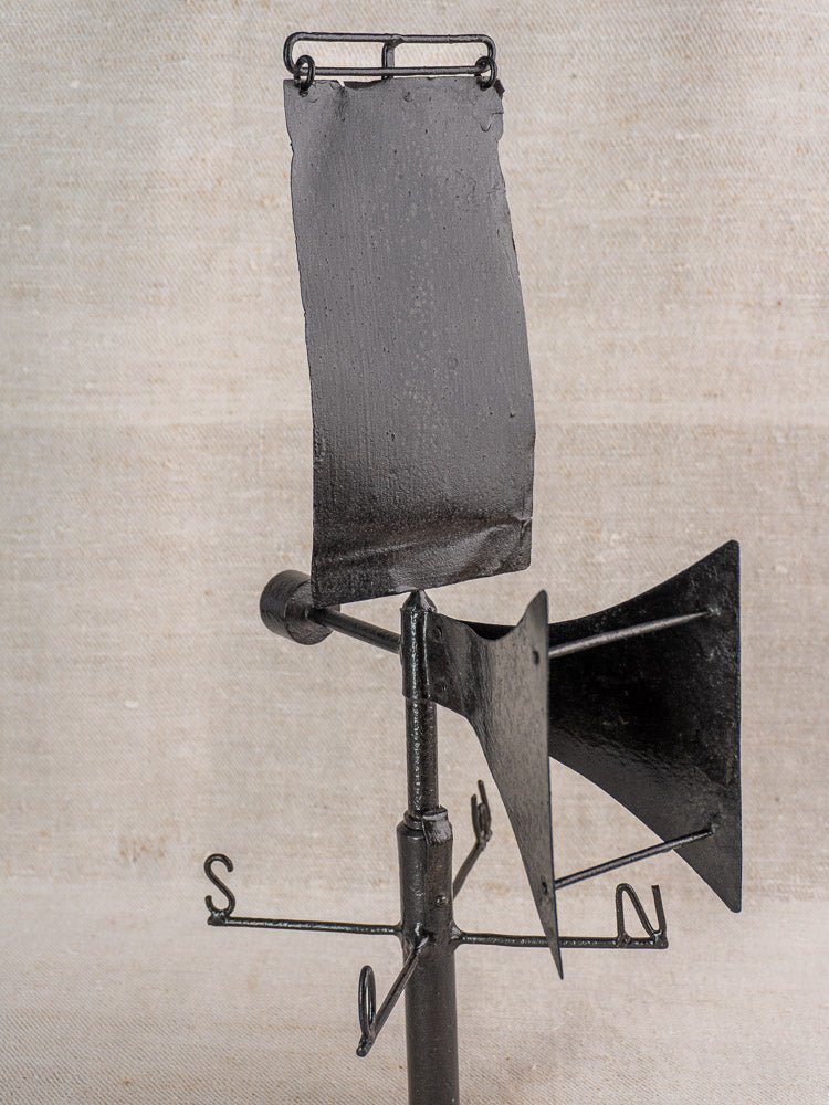 Antique French painted iron weathervane with V-shaped front, black finish, on beige fabric background.