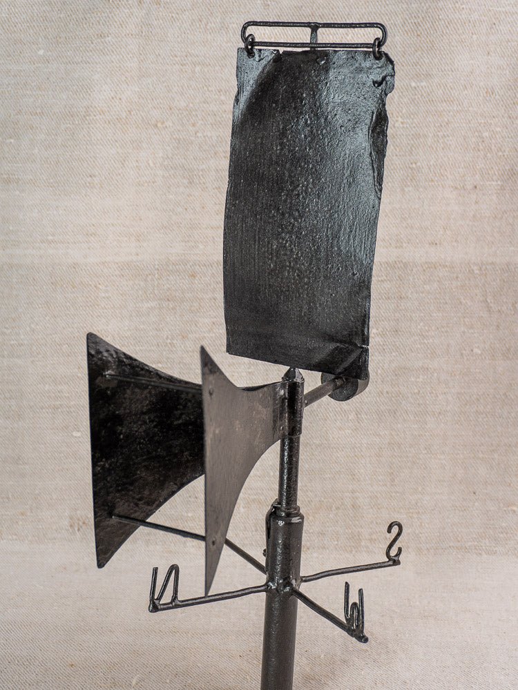 Antique French painted iron weathervane with arrow and compass points on beige textured background.