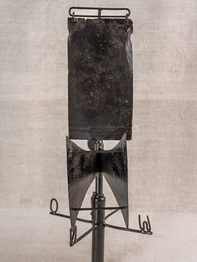 Antique French painted iron weathervane with fan-shaped wings on metal rod, beige textured background.