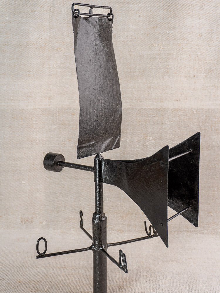 Antique French painted iron weathervane with rooftop girouette design and compass points on beige background.
