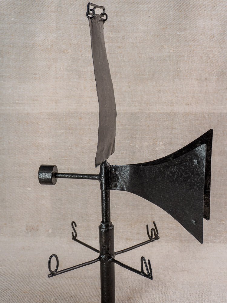 Antique French painted iron weathervane with horn-shaped front and cardinal compass, on pole, beige fabric backdrop.