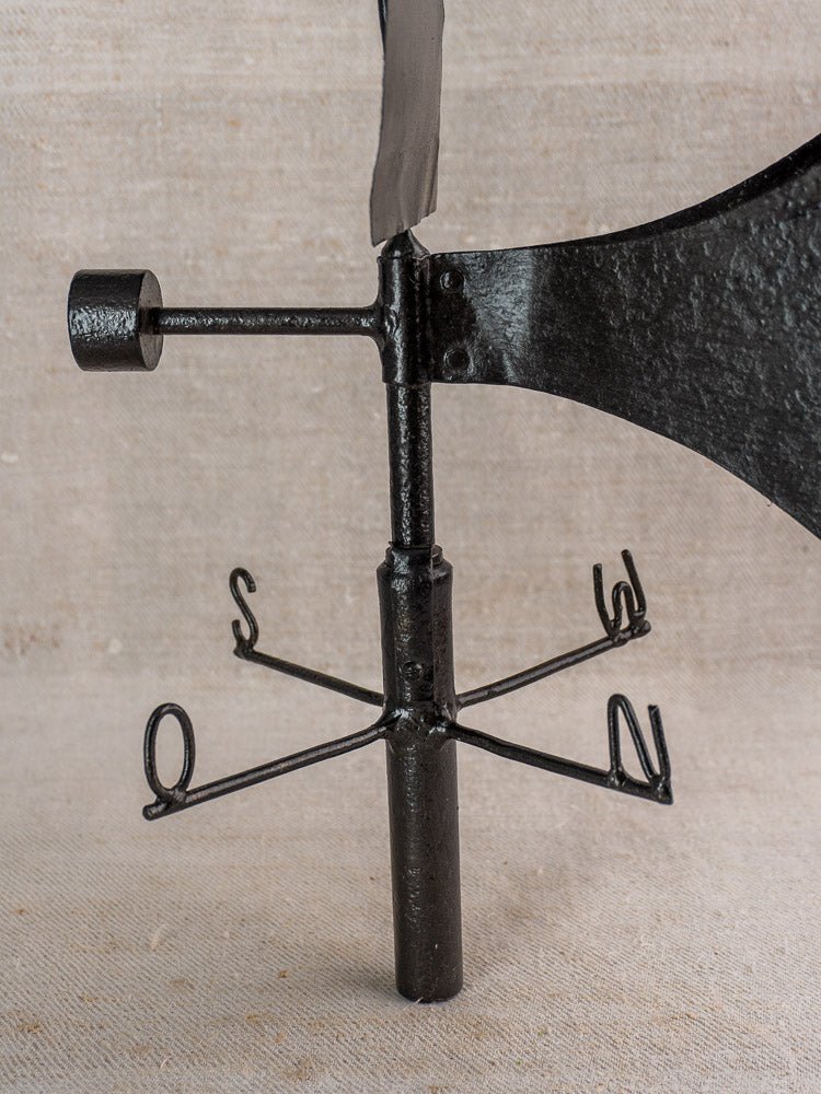 Antique French painted iron weathervane with N, S, E, W letters on beige fabric background.