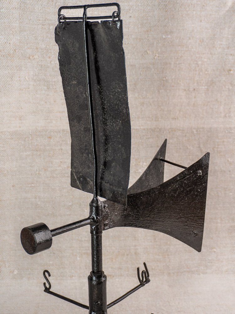 Antique French painted iron weathervane with cardinal compass, rustic finish, on beige fabric background.