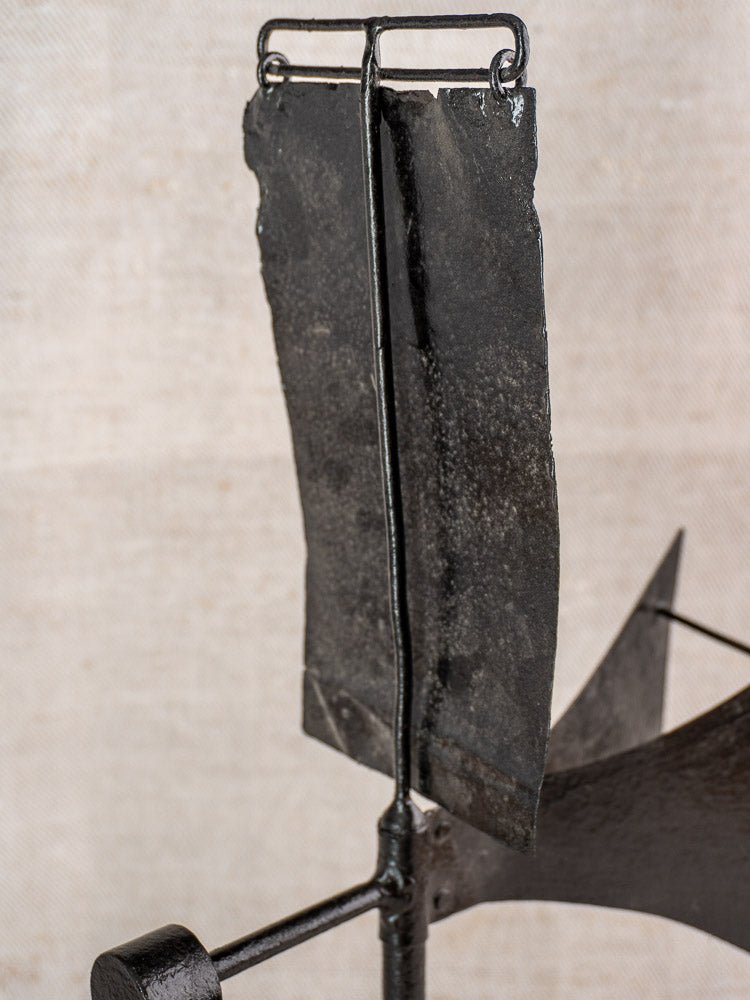 Antique French painted iron weathervane with cardinal compass, jagged-edged vertical form, beige textured backdrop.