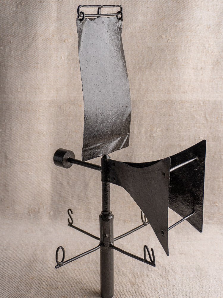 Antique French painted iron weathervane with cardinal compass, displayed on beige textured fabric background.