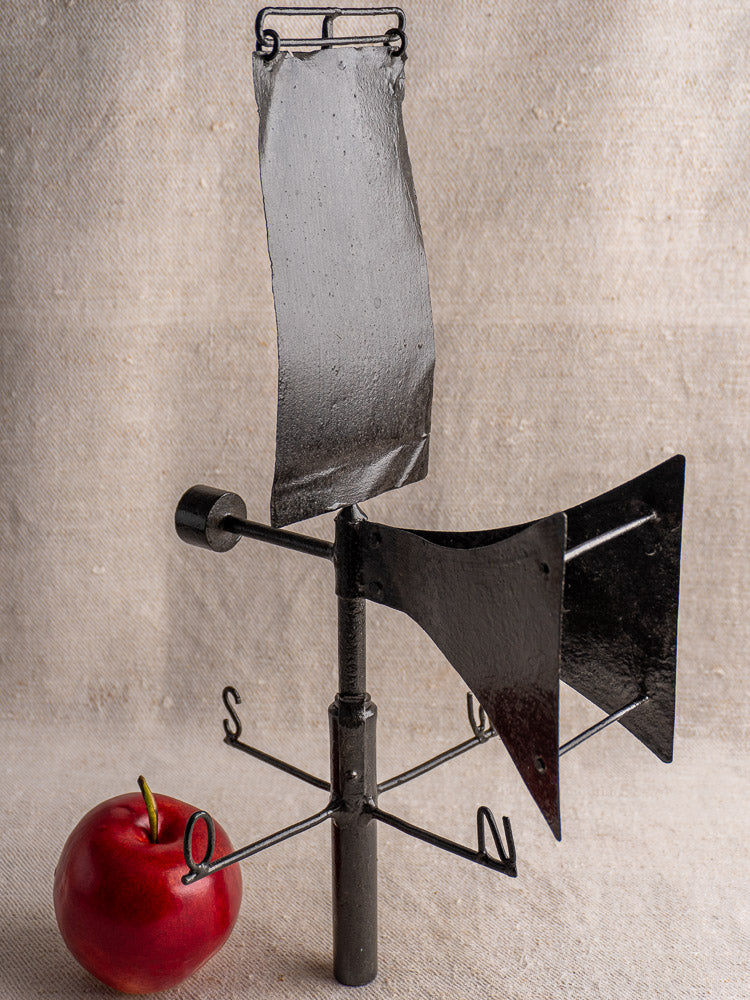 Antique French painted iron weathervane with V-shaped front, black finish, on beige fabric background.