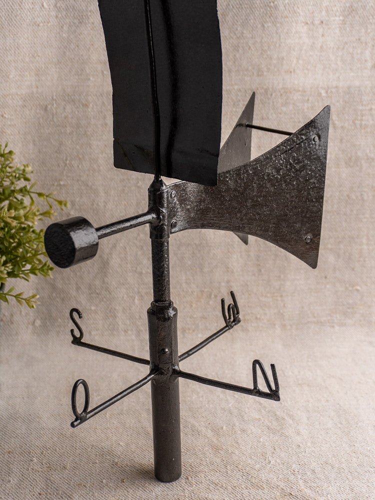 Antique French painted iron weathervane with cardinal compass, bold black arrow, on neutral fabric background.
