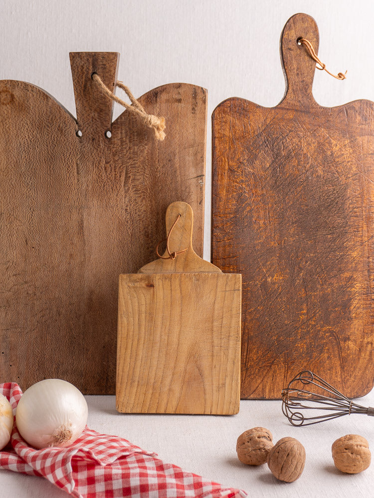 Vintage French bread board (mid 20th century) with onion, walnuts, whisk, and checkered cloth on white surface.