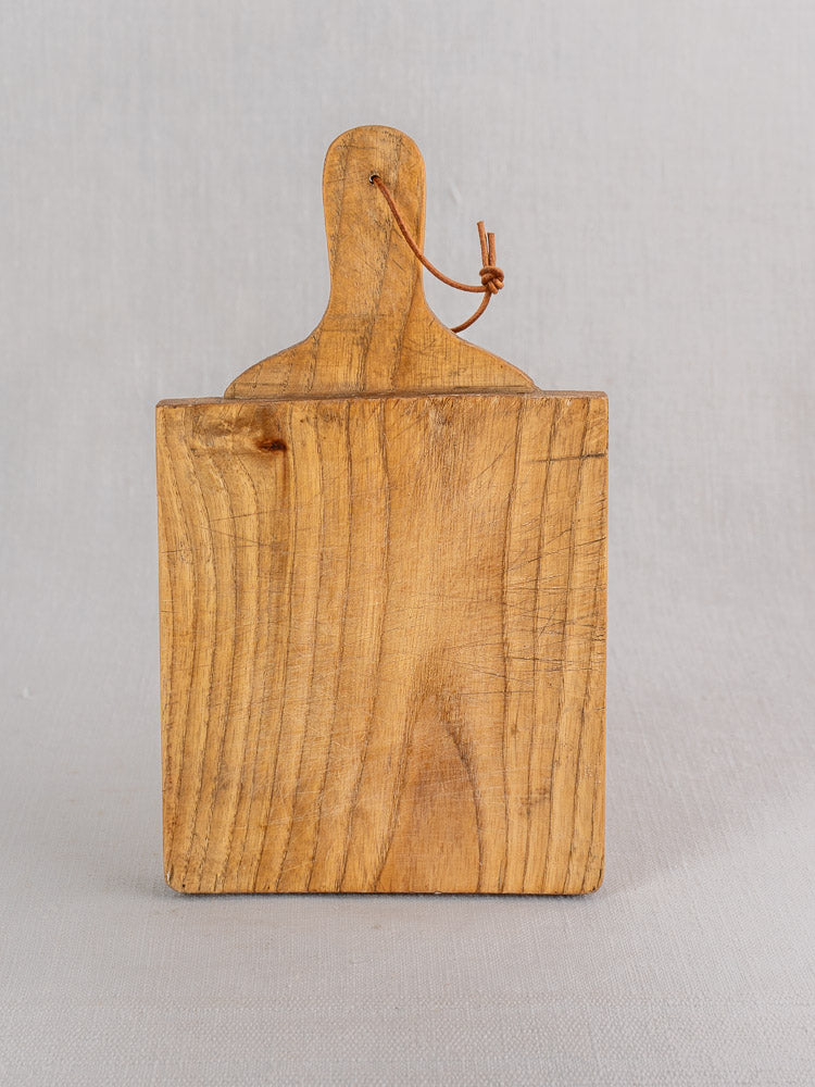 Small rectangular oak French bread board with handle and leather loop, inspired by antique boards, on light gray background.
