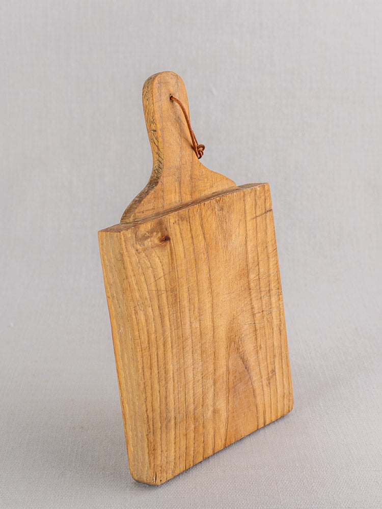 Mid-century French oak bread board with handle and looped cord, standing upright on a light gray background.
