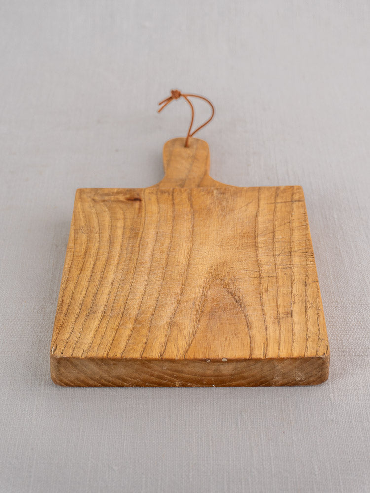 Small mid-century French oak bread board with short loop handle on a light gray surface.