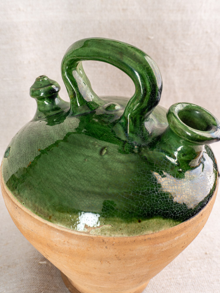 Antique French gargoulette with emerald green-glazed handle and spouts, beige clay base, on neutral textured background.
