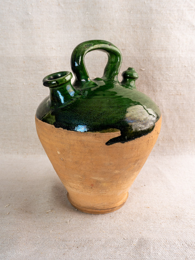 Antique French gargoulette with looped handle, dual spouts, emerald green glaze, on linen background.