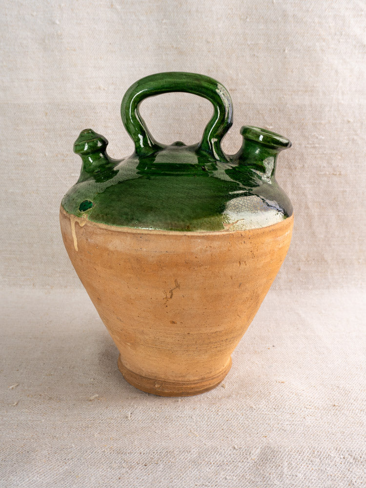 Antique French gargoulette, 19th century, natural clay and emerald green glaze, two spouts, central handle, on neutral fabric.