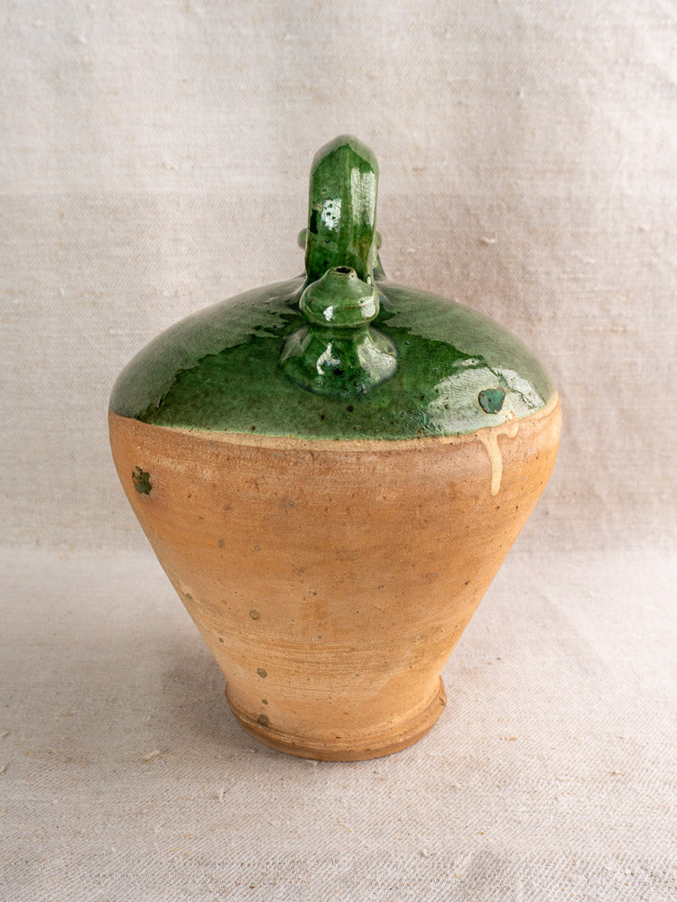 Antique French gargoulette with wide base, narrow top, and emerald green glaze, set on light textured fabric.