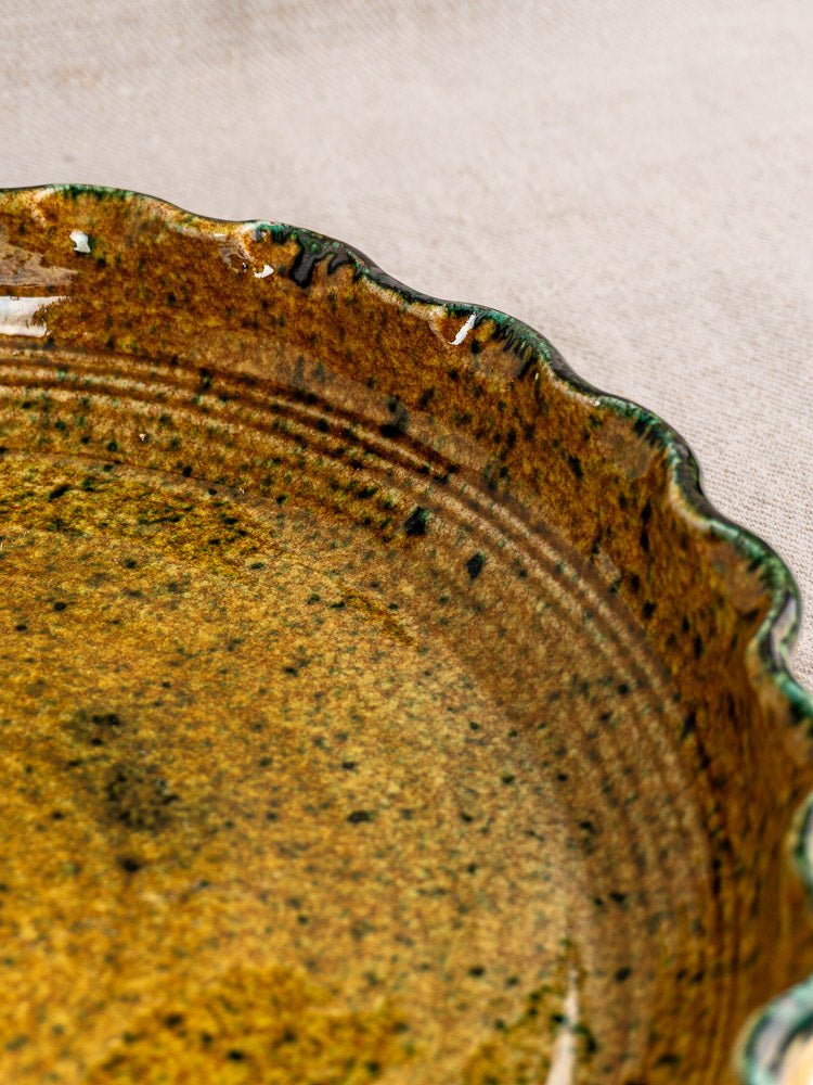 Vintage French JANY Studio earthenware tarte dish with scalloped edge, brown and green glaze, on fabric background.