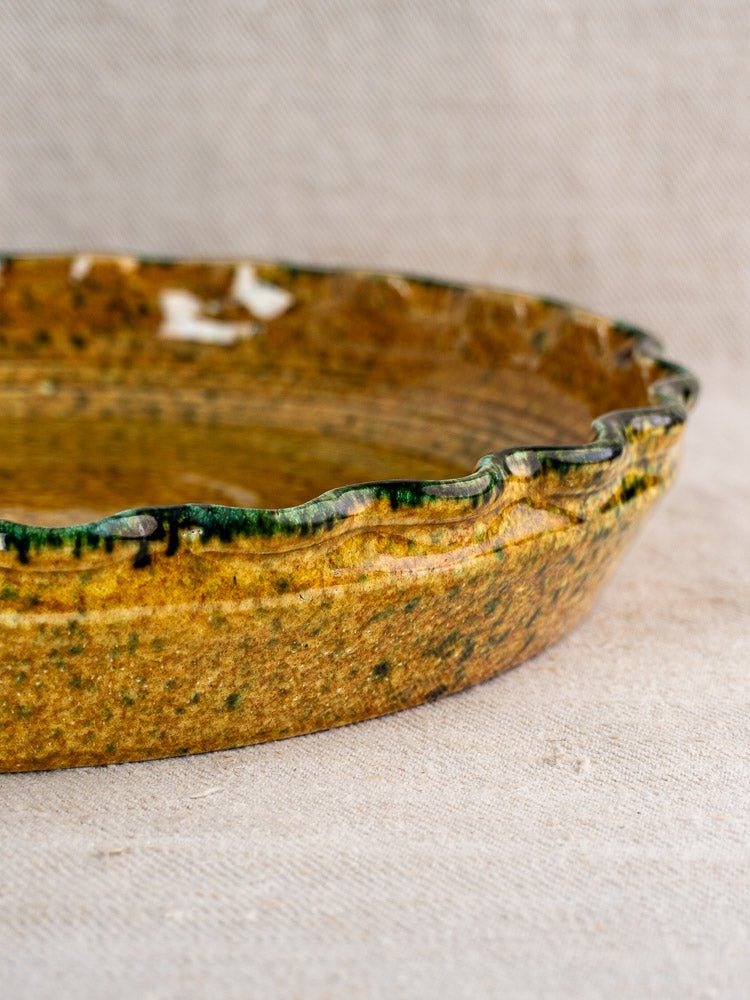 Vintage French JANY Studio tarte dish, round earthenware with rustic green-brown glaze, fluted edge on beige fabric.