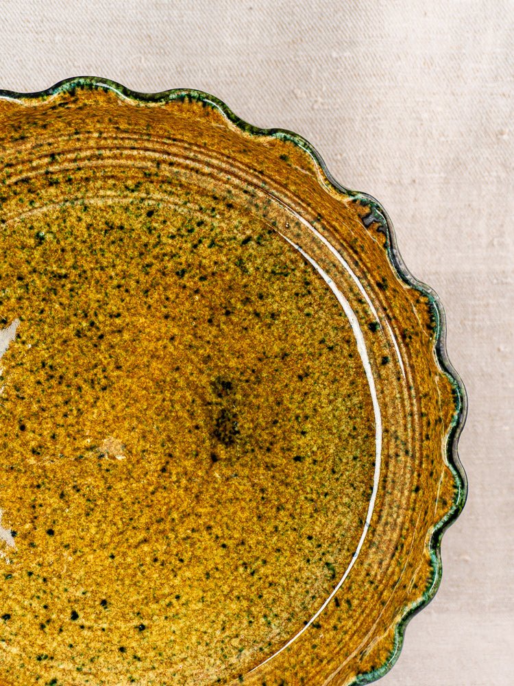 Vintage French signed JANY Studio earthenware tarte dish with scalloped edge, brown speckled glaze on beige fabric.