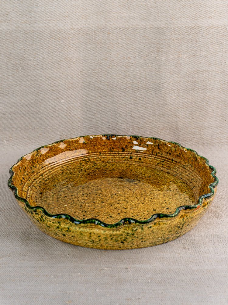 Yellow and green ceramic dish with scalloped edge, JANY Studio signature, on beige textured surface.