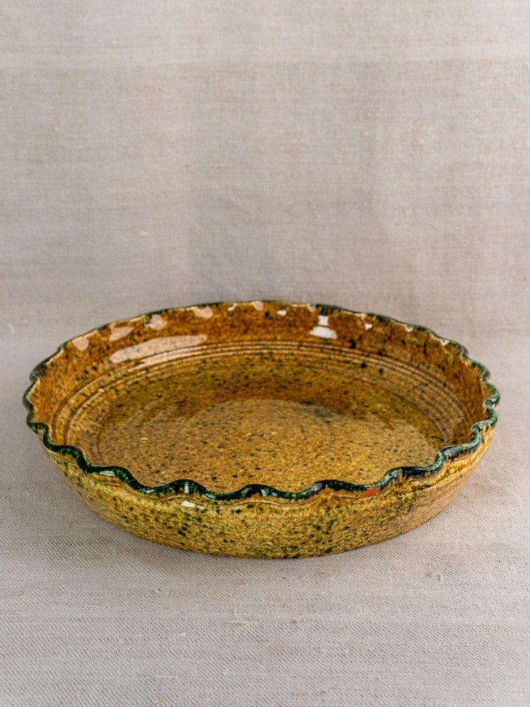Vintage French JANY Studio earthenware tarte dish with scalloped edge and mottled yellow-brown glaze on neutral fabric.