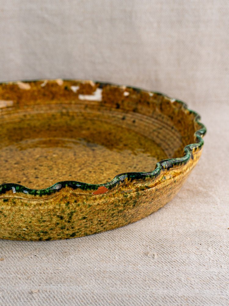 Vintage French signed JANY Studio earthenware tarte dish with scalloped rim and mottled glaze on beige fabric.