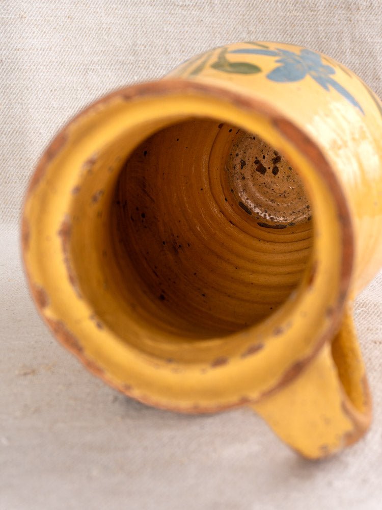 Antique French yellow glazed ceramic pitcher with handle, showing textured floral earthenware interior, on fabric.