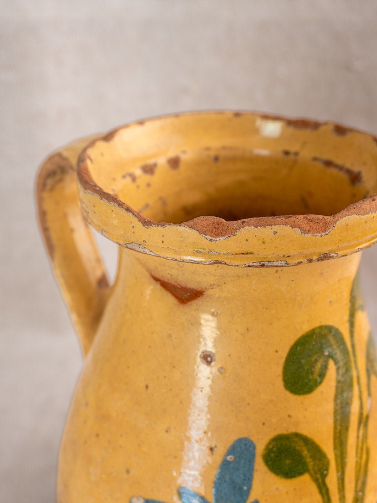 Antique French yellow glazed ceramic pitcher with wavy rim, sturdy handle, and hand-painted floral motifs.
