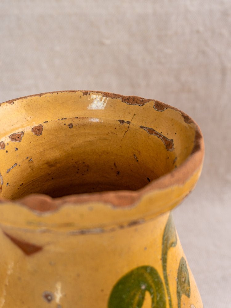 Weathered yellow-glazed rim of French hand-painted earthenware pitcher with terracotta clay exposed, on linen background.