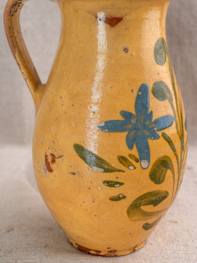 Antique French yellow glazed ceramic pitcher with hand-painted blue flowers, green leaves, and vintage wear.