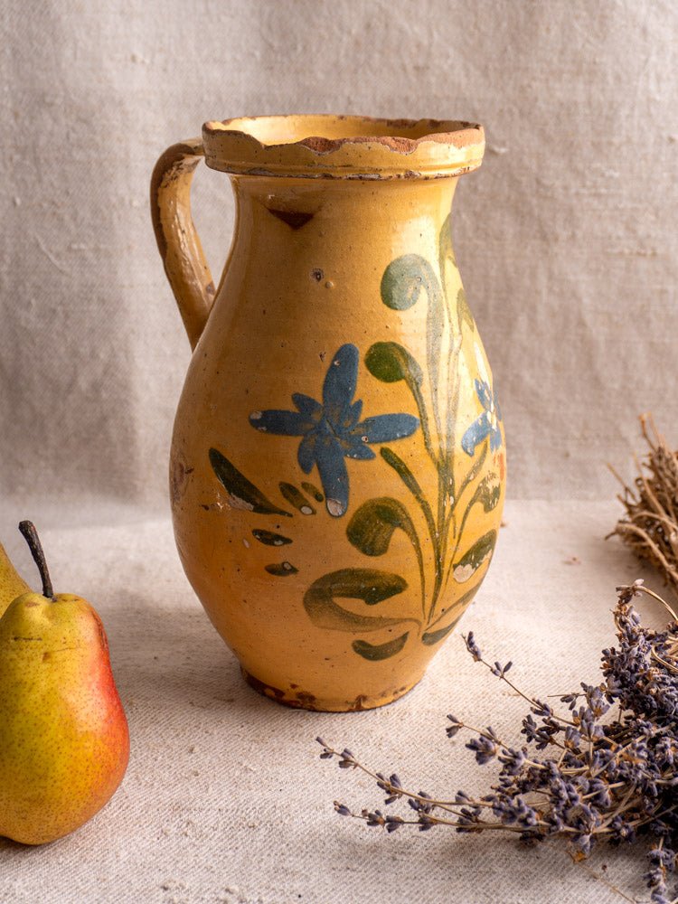 Antique French yellow glazed earthenware pitcher with hand-painted florals beside a pear and dried lavender.