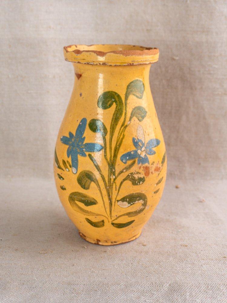 Antique French yellow glazed ceramic pitcher with hand painted blue flowers and green leaves, on neutral fabric.