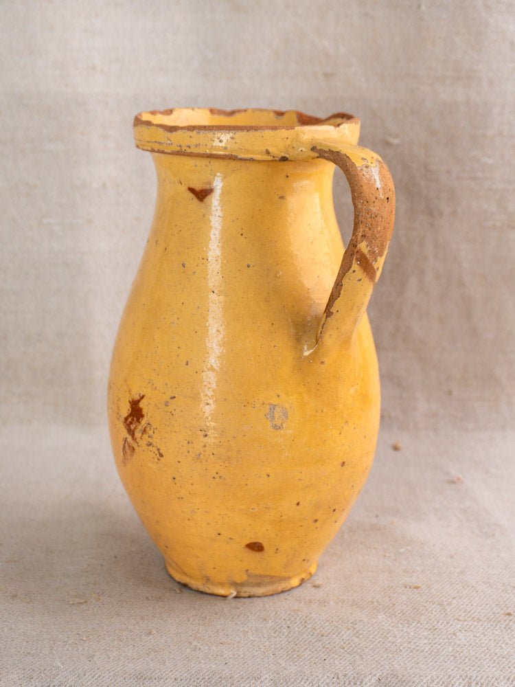 Antique French yellow glazed earthenware pitcher with floral motifs and single handle, on textured fabric.