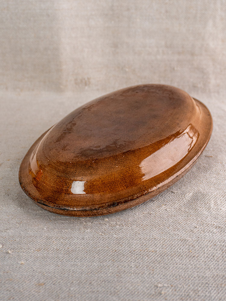 Antique French Provençal Tian gratin dish with crackle glaze, displayed upside down on textured light fabric.