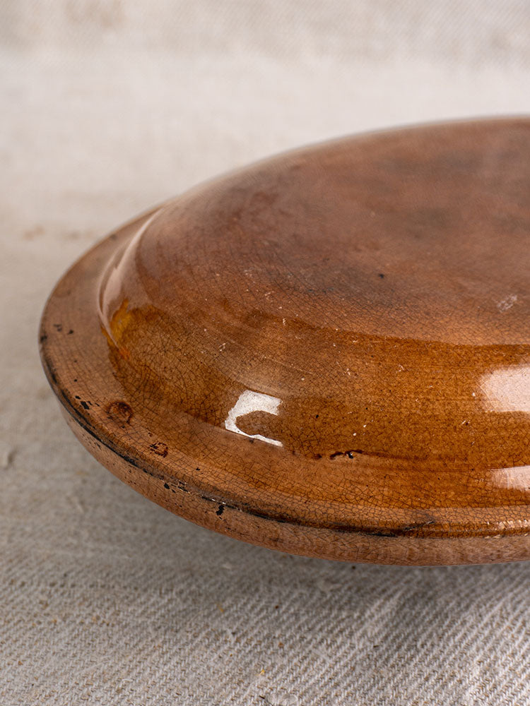 Underside of antique French gratin dish with crackle glaze and glossy finish on beige fabric.