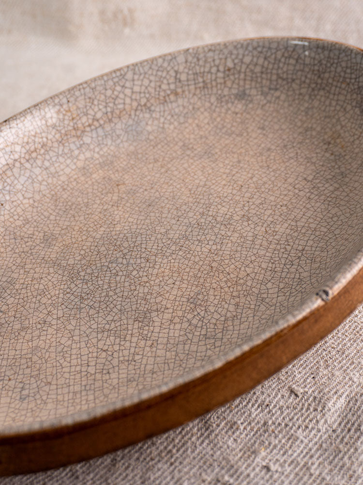 Antique French gratin dish with crackle glaze and brown rim in Provençal Tian style on beige fabric.