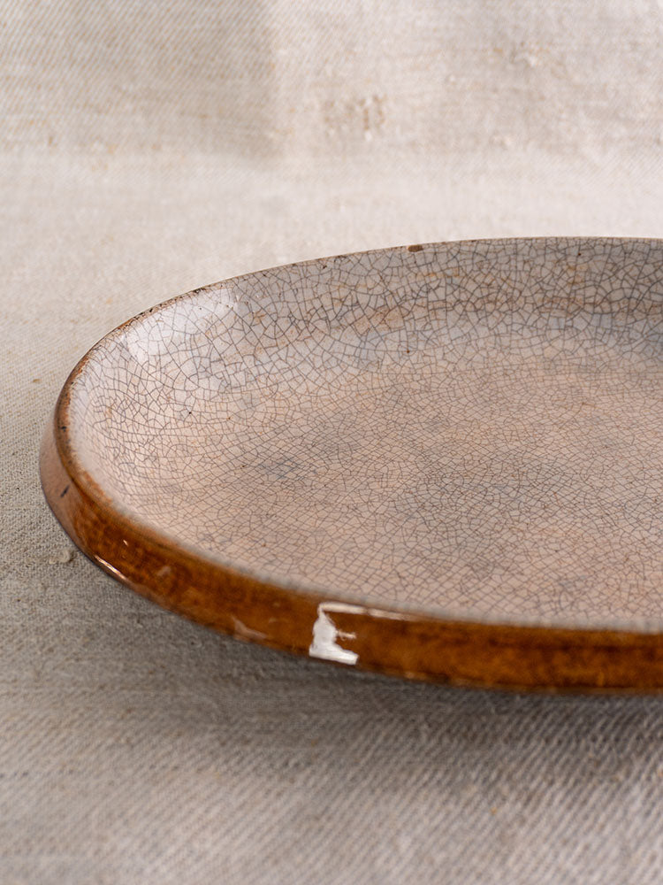 Antique French Provençal Tian gratin dish with crackle glaze and brown rim on textured beige fabric.