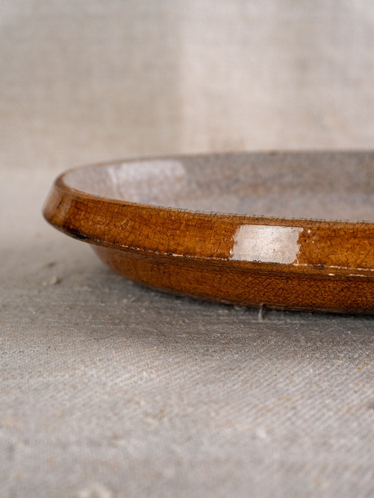 Antique French gratin dish with crackle glaze, glossy brown rim, and textured interior on neutral fabric surface.