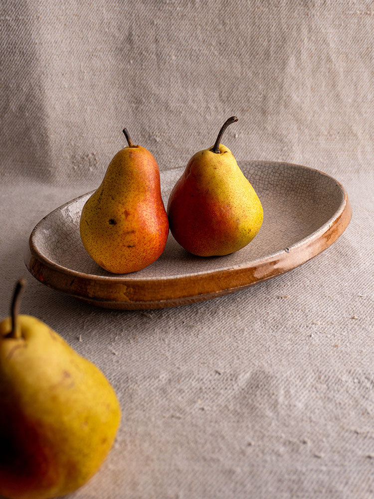 Antique French gratin dish with crackle glaze, brown rim, and textured gray interior on neutral fabric.