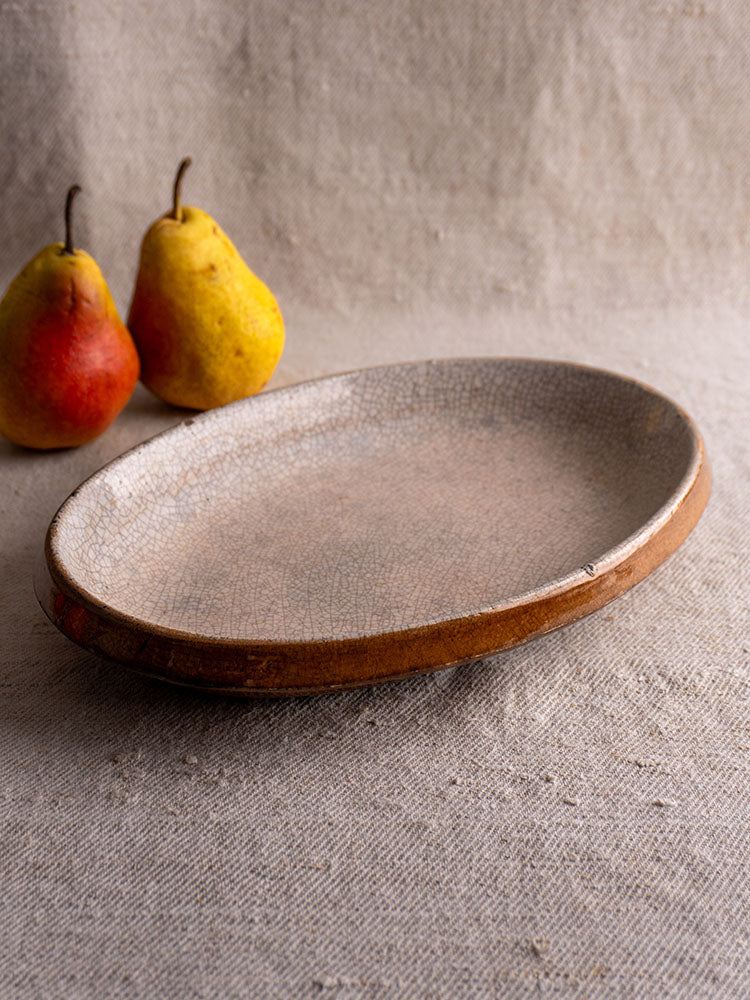 Antique French gratin dish with crackle glaze and brown rim, Provençal Tian style, on beige fabric, pears in background.