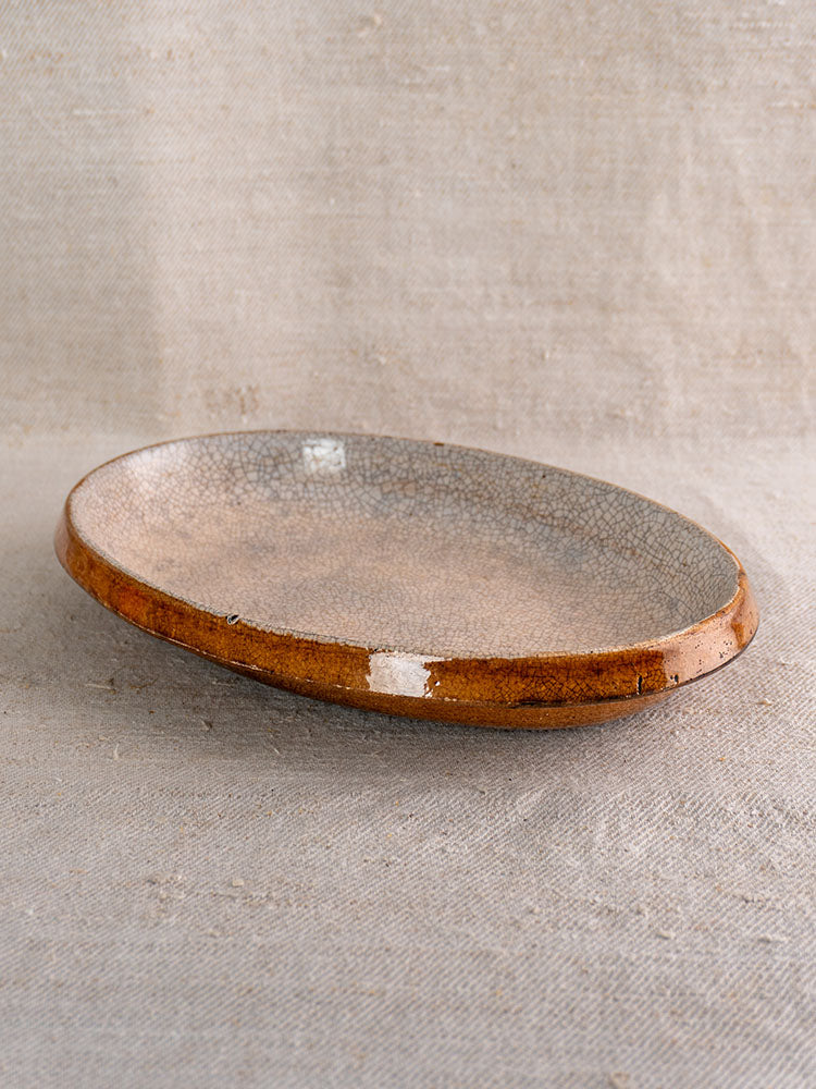 Antique French gratin dish with crackle glaze, brown rim, and textured gray interior on neutral fabric.