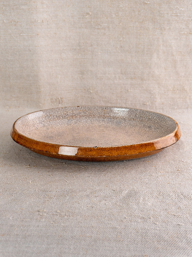 Antique French gratin dish in Provençal Tian style with crackle glaze and glossy brown rim on beige textured fabric.